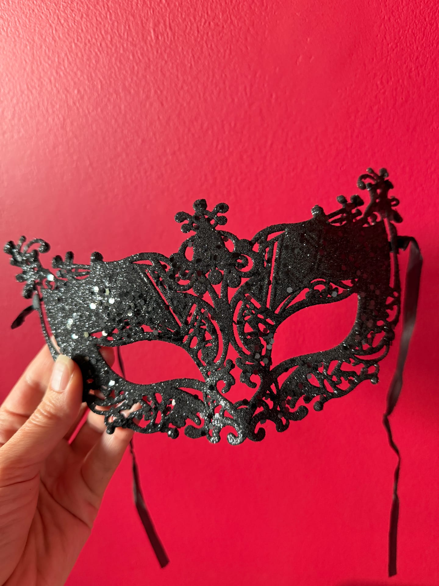 An ornate black filigree masquerade mask held against a deep red wall