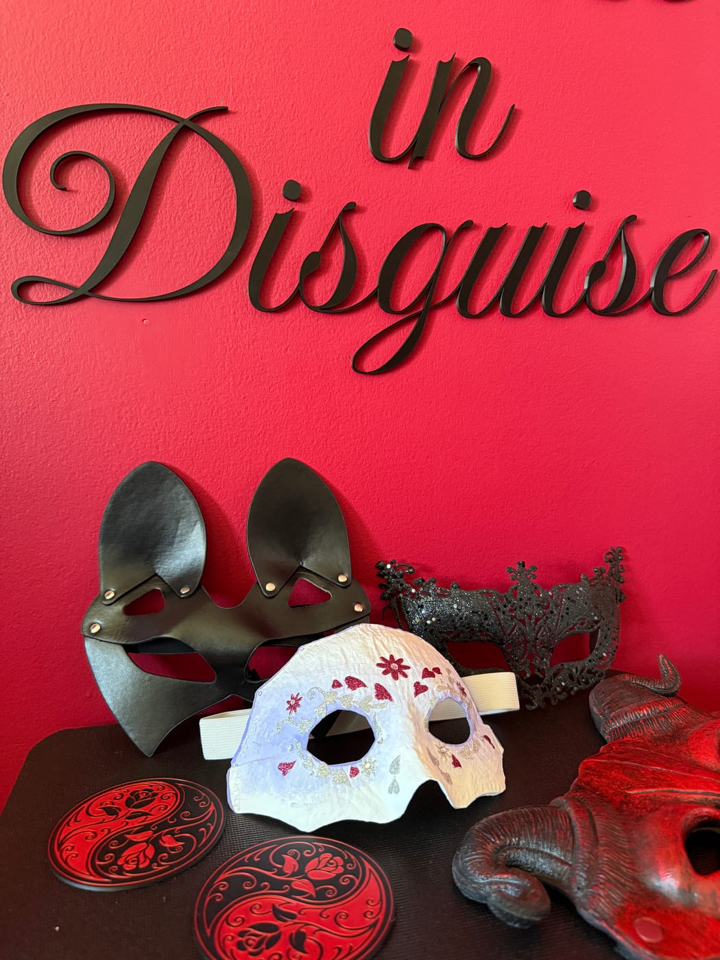 A collection of masks — leather, lace, and ceramic — against the studio's deep red wall